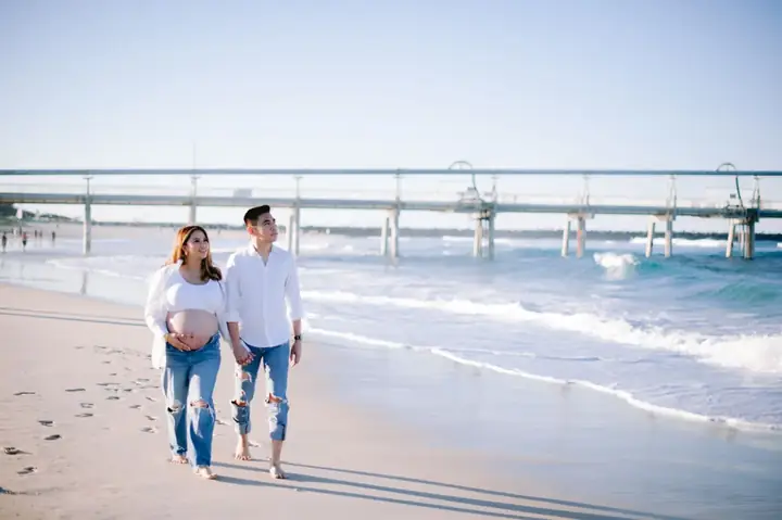 An expectant couple walking together on the beach